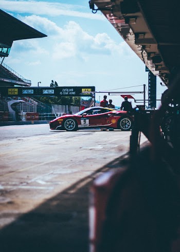 Red Racing Car on Racing Field Near Three Man Standing Under White Clouds and Blue Sky