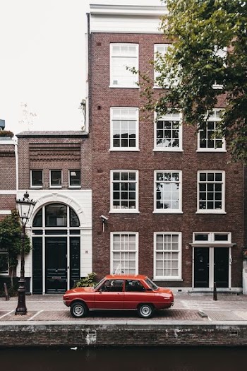 red sedan parking beside high-rise building at daytime