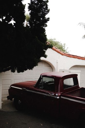 red single cab pickup truck parked beside white house under white sky at daytime