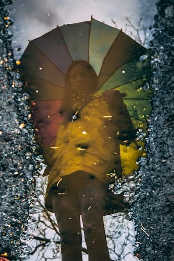 reflection photography of woman standing while holding umbrella