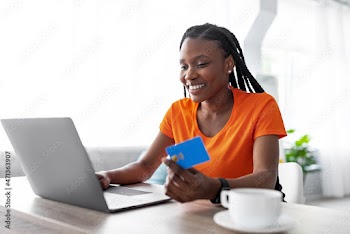 Remote shopping. Cheery black lady using laptop and credit card to order goods on web from home, free space