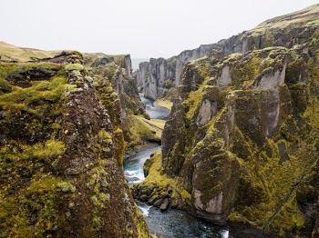 river in the middle of rock cliff with moss