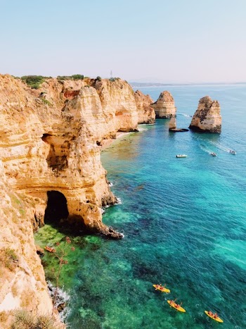 Rock Cliff Near Ocean With Kayakers and Speed Boat Passing