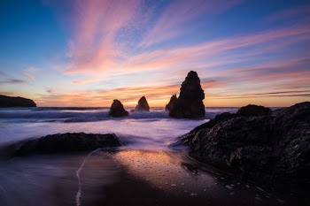 rock monument beside water with cloudy sky