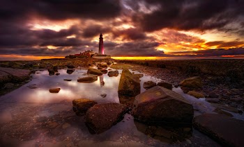 Rocks on Body of Water Near Lighthouse during Golden Hour