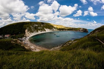round beach near green mountain under white clouds at daytime