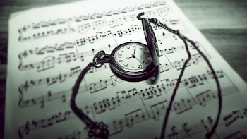 Round Gray Pocket Watch Reading 11:15 Placed on Music Sheet