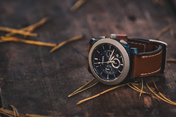 Round Silver Colored Fossil Chronograph Watch With Brown Leather Band On Brown Wooden Surface