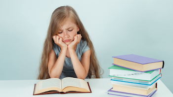 Sad girl 7-8 years old reading book on the table and looking at ...