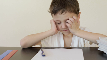 Sad little boy sitting at the table and doing homework. Concept of ...