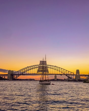 Sail Boat in Front of Bridge Under Orange Sunset