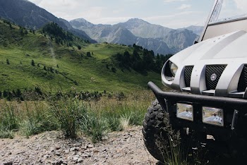 Scenic View Of Lush Green Mountains With A Vehicle Parked On A Unpaved Pathway