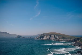 sea waves beside gray and green cliff under clear blue sky during daytime