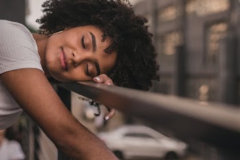 Selective Focus Close-up Photo of Smiling Woman with Her Eyes Closed Resting Hand and Head on Metal Railing