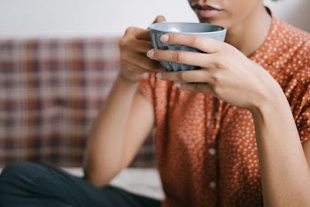 Selective Focus Close-up Photo of Woman in Orange Top Holding Gray Cup