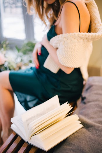 Selective Focus of Pregnant Woman in Black Spaghetti Strap Dress Sitting on Chair Beside Opened Book
