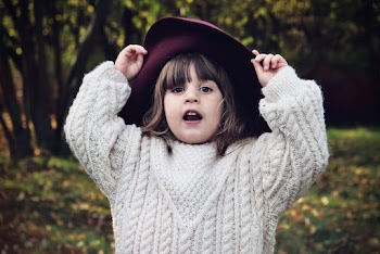 Selective Focus of Small Girl in Maroon Hat and White Knitted Sweater Posing