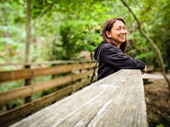 Selective Focus of Smiling Woman in Black Hoodie Leaning on Wooden Railing