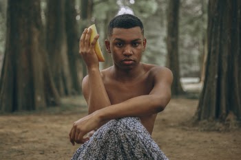 Selective Focus of Topless Man Sitting Holding Slice of Fruit Surrounded by Trees