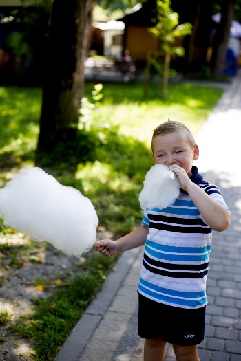 Selective Focus Photo of Boy Eating Cotton Candy with His Eyes Closed Standing on Side Walk