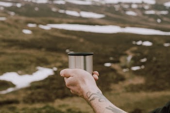 Selective Focus Photo of Man's Hand Holding Out a Stainless Steel Cup