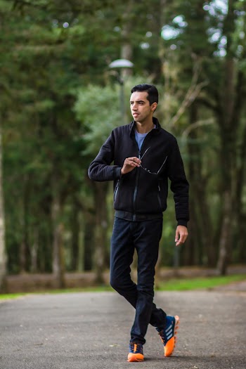 Selective Focus Photo of Man in Black Jacket and Pants Standing on Road Posing While Holding Glasses and Looking Away