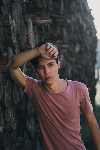 Selective Focus Photo of Man in T-shirt Leaning on Wood Logs Posing