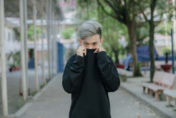 Selective Focus Photo of Man Posing While Covering His Mouth with a Black Sweater