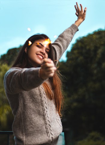Selective Focus Photo of Smiling Woman Holding a Lit Sparkler Posing With Her Hand Up