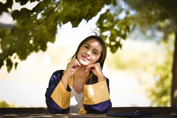 Selective Focus Photo of Smiling Woman in Academic Regalia Leaning on Wooden Railing With Her Hands on Her Chin