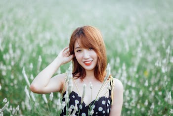 Selective Focus Photo of Smiling Woman in Black Floral Dress Standing Alone in Grass Field