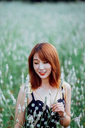 Selective Focus Photo of Smiling Woman in Black Floral Top Standing Alone in Grass Field