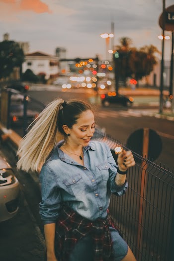 Selective Focus Photo of Smiling Woman in Blue Denim Outfit Standing Near Black Metal Fence