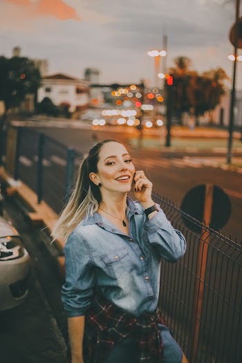Selective Focus Photo of Smiling Woman in Blue Denim Outfit Standing Near Black Metal Fence