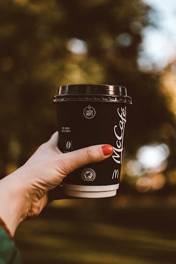 Selective Focus Photo of Woman's Hand Holding Out a McCafe Cup of Coffee