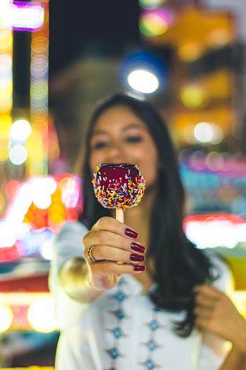 Selective Focus Photo of Woman Holding Out a Candy Apple