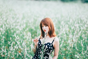Selective Focus Photo of Woman in Black Floral Dress Standing Alone in Grass Field Posing With Her Eyes Closed