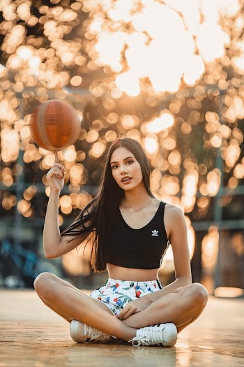 Selective Focus Photo of Woman in Black Top and White Floral Shorts Spinning Basketball on Finger While Sitting Down