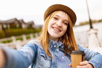 Selective Focus Photo of Woman in Blue Denim Jacket Holding Coffee Cup While Smiling