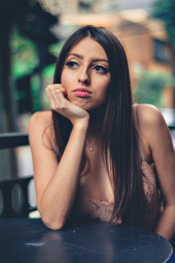Selective Focus Photo of Woman in Brown Top Leaning on Table with Her Hand on Her Chin