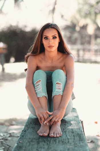 Selective Focus Photo of Woman in Denim Jeans Sitting on Bench with Her Legs Up Close to Her Chest