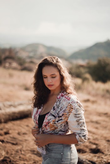 Selective Focus Photo of Woman in Floral Top and Blue Jeans Posing While Looking Down