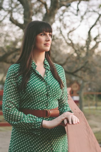 Selective Focus Photo of Woman in Green and White Polka-dot Long-sleeved Dress Standing Near Wooden Railing Looking into the Distance