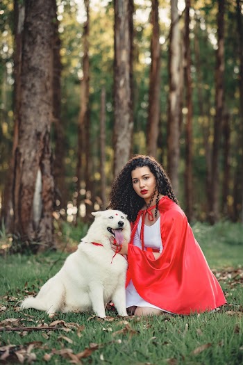 Selective Focus Photo of Woman in Red Cape and White Dress Kneeling Beside White Dog