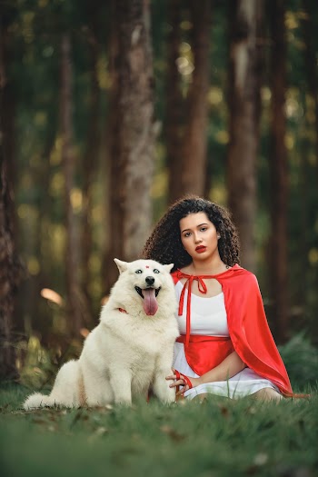 Selective Focus Photo of Woman in Red Cape and White Dress Sitting Beside White Dog