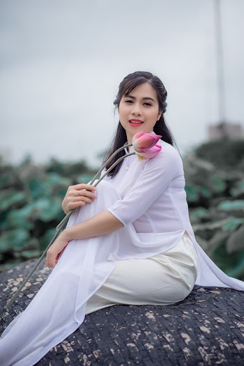 Selective Focus Photo of Woman in White Sheer Top Holding a Pink Lotus Flower
