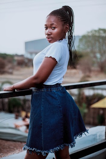 Selective Focus Photo of Woman in White Top and Blue Denim Skirt Posing by Wooden Railing