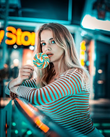 Selective Focus Photo of Woman Leaning on Metal Railing While Holding Lollipop Posing