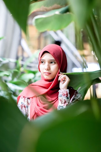 Selective Focus Photo of Woman Wearing Red Hijab Standing Near Green Plants
