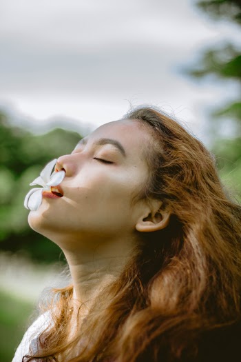 Selective Focus Photo of Woman With a White Flower in Her Mouth Posing with Her Eyes Closed